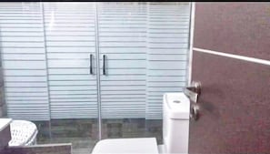 A room with a sliding glass door leading to a balcony, a white toilet, and a small trash bin.