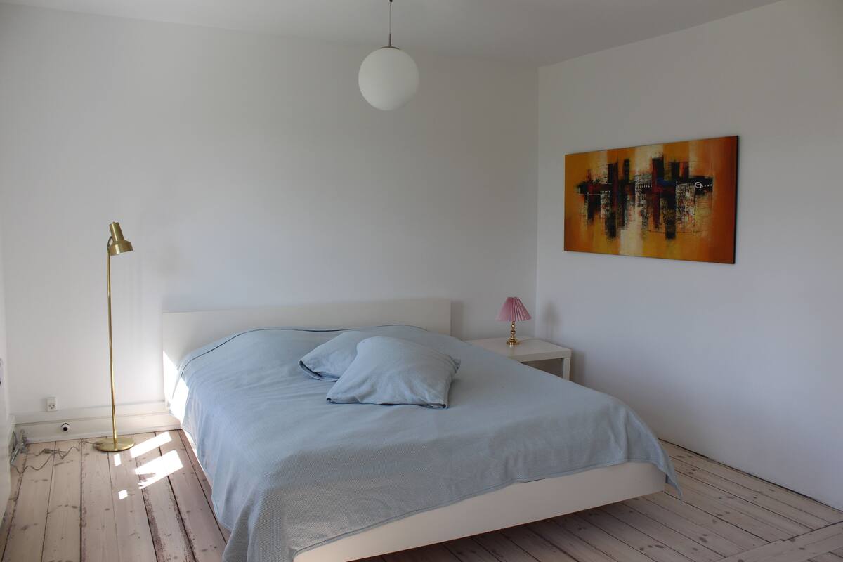 Ein Schlafzimmer mit einem Bett, einem Nachttisch, einer Lampe und einem Gemälde an der Wand.