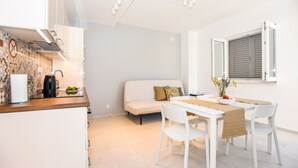 A compact kitchen with a dining area, a sofa, and a window with blinds. - Apartments Villa Magena (Pag)