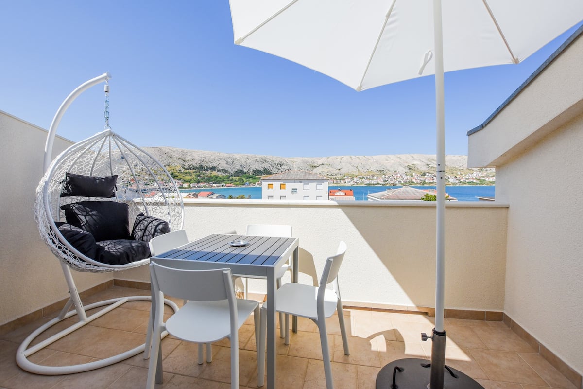 A balcony with a white table, chairs, a hanging chair, and a large umbrella.