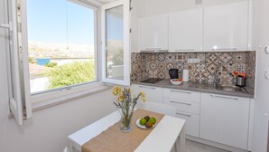 A modern kitchen with white cabinets, a tiled backsplash, and a window overlooking a scenic view. - Apartments Villa Magena (Pag)