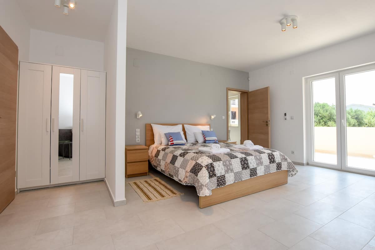 A modern bedroom with a large bed, a wardrobe, and a sliding glass door to a balcony.