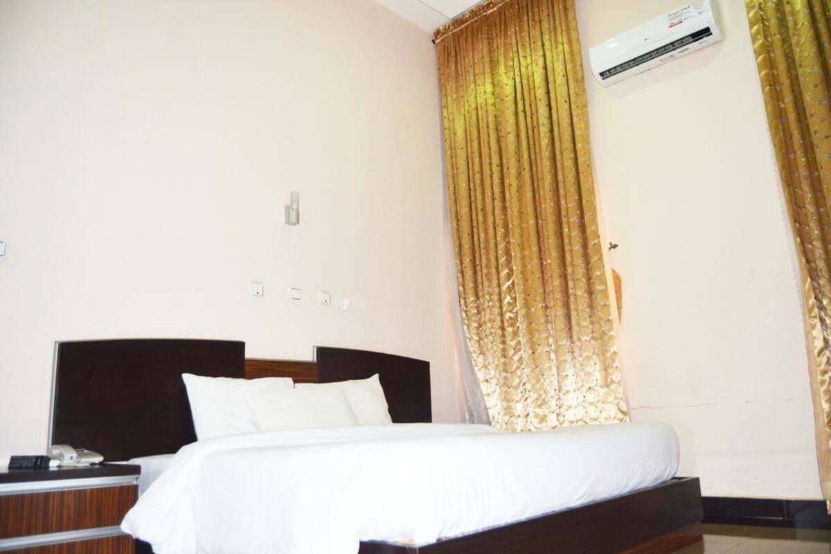 A hotel room with a large bed, a bedside table with a phone, and a wall-mounted air conditioner.