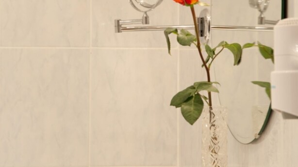A bathroom with a white marble wall, a round mirror, and a vase with a single orange rose. - Double room I - Guesthouse Zibert (Rottach-Egern)