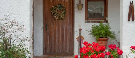 A white-walled building with a wooden door, a window, and a potted plant with red flowers.