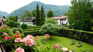 A garden with neatly trimmed hedges, a lawn, and outdoor seating. - Double room I - Guesthouse Zibert (Rottach-Egern)