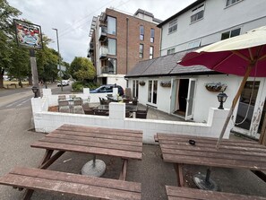 An outdoor seating area with wooden tables and benches, a white building with a red umbrella, and a sign for 'Watermans Arms'.