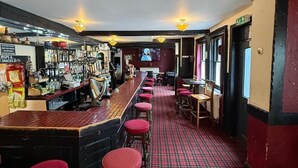 Een bar met krukken, een toog en een televisiescherm.