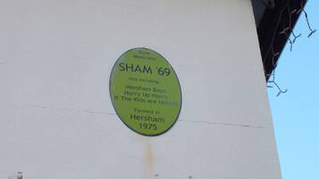 A green plaque on a building wall with text about a band named SHAM '69, formed in 1975 in Hersham.