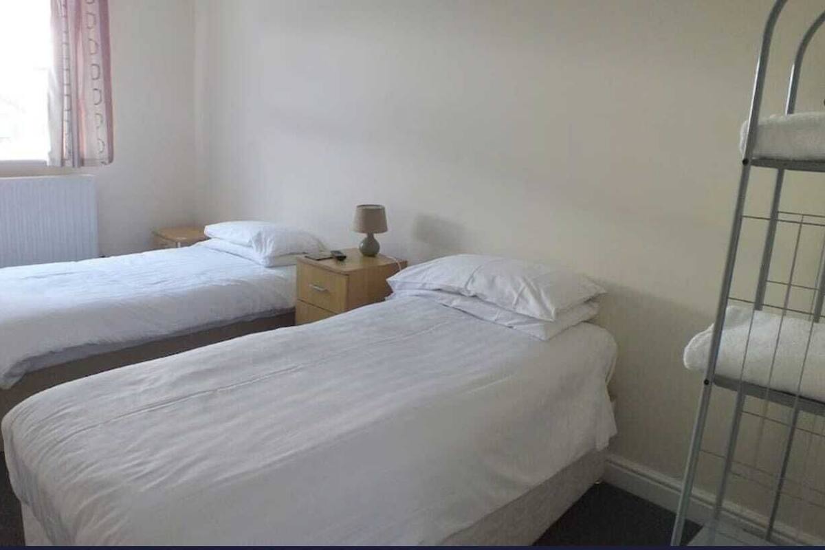 Een hotelkamer met twee enkele bedden, een nachtkastje met een lamp en een raam met gordijnen.