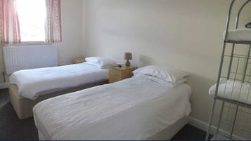 Habitación de hotel con dos camas individuales, una mesita de noche con lámpara y una ventana con cortinas.