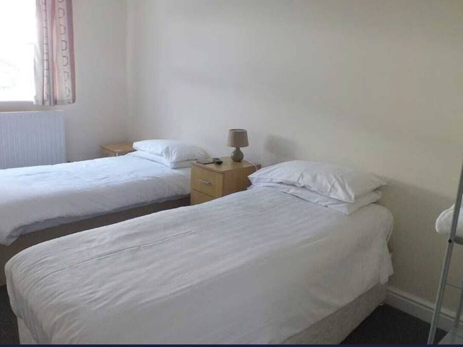 Habitación de hotel con dos camas individuales, una mesita de noche con lámpara y una ventana con cortinas.