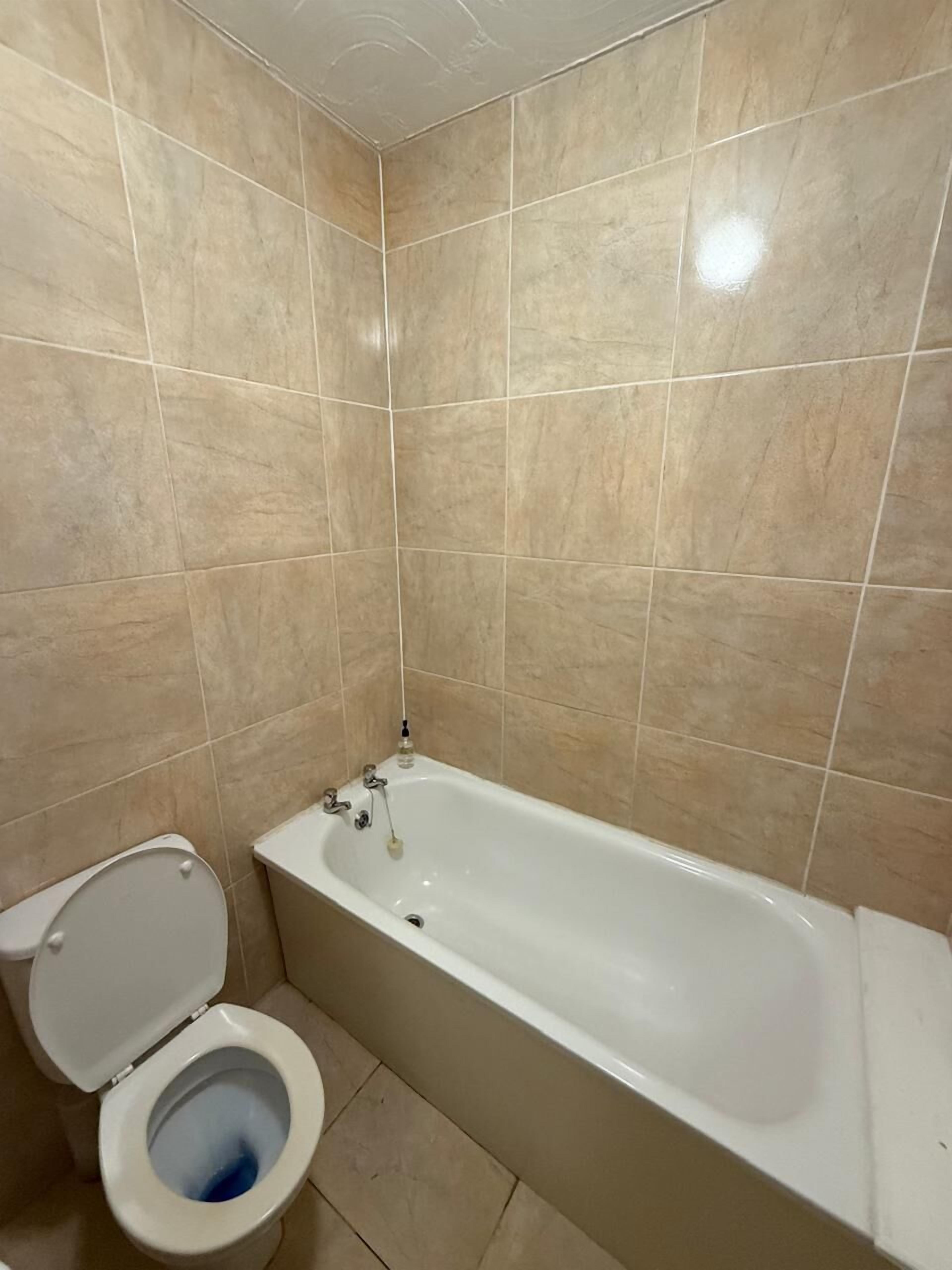 A bathroom with beige tiled walls and a white bathtub.