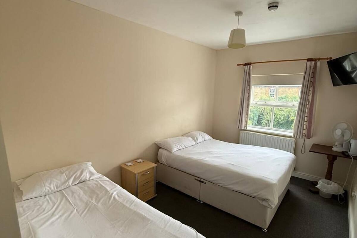 Een hotelkamer met twee bedden, een klein houten nachtkastje, een bureau met stoel, een aan de muur bevestigde televisie en een raam met gordijnen.