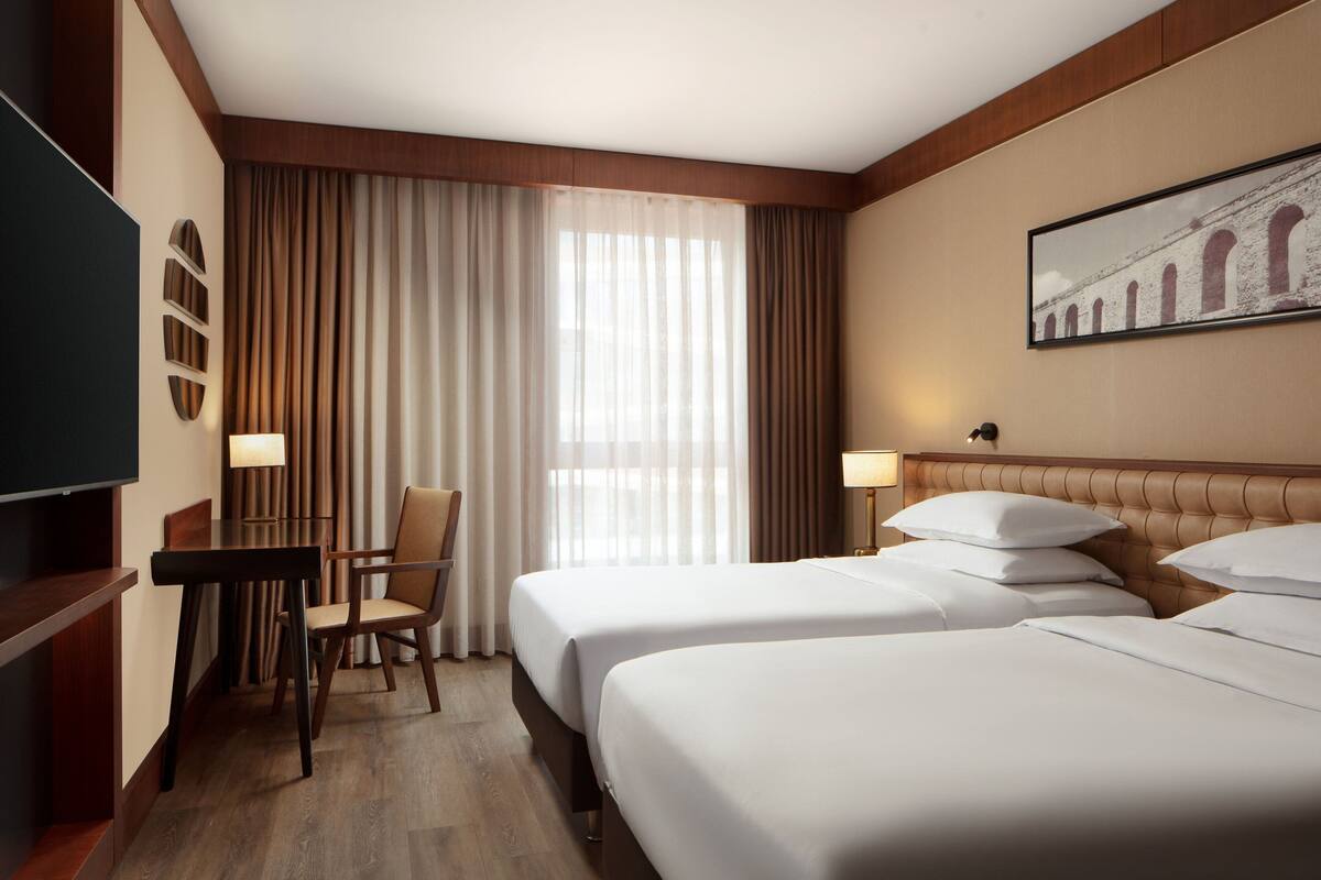 Habitación de hotel con dos camas, un escritorio, una silla y un televisor.