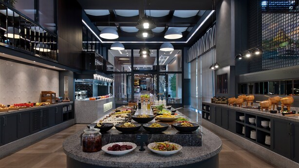 A modern hotel lobby with a central buffet area featuring a variety of food items. - Sheraton Istanbul City Center (Istanbul)