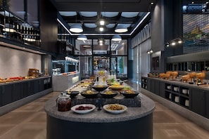 Un moderno vestíbulo de hotel con una zona de buffet central que ofrece una variedad de alimentos.