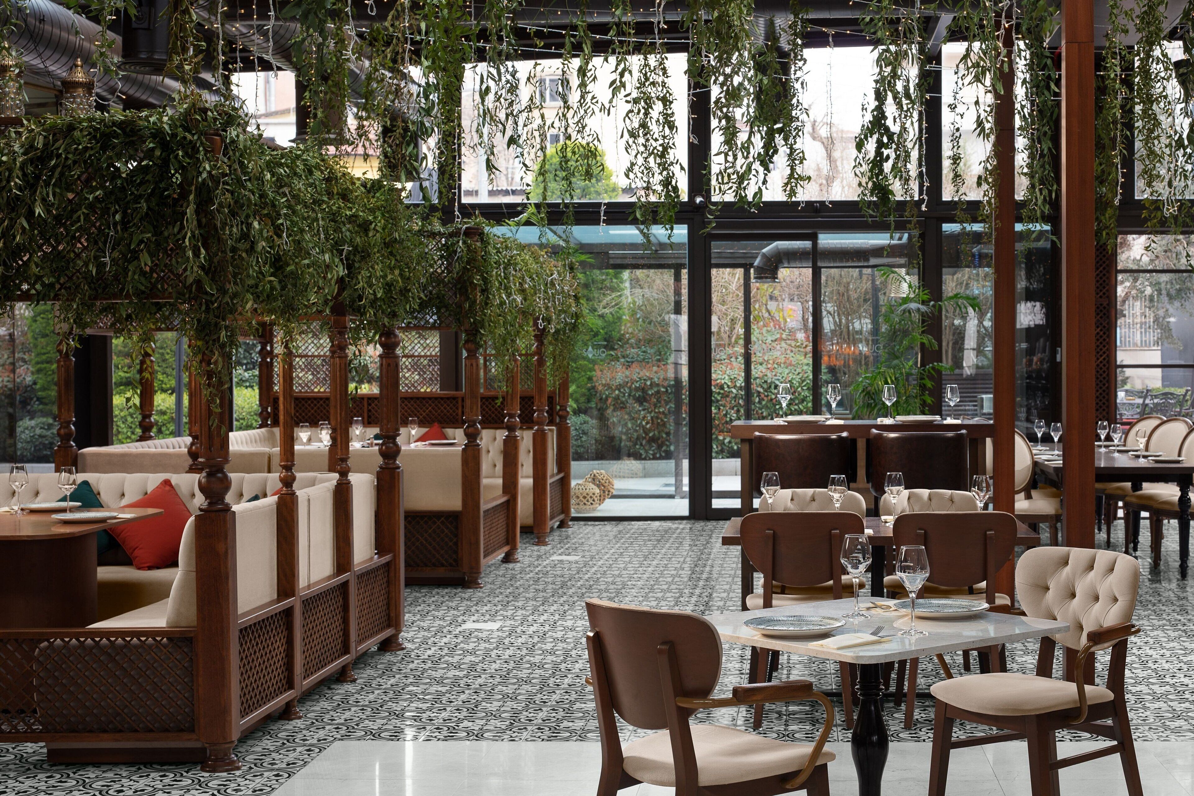 Un restaurant avec une salle à manger intérieure, des plantes suspendues et une vue sur l’extérieur.