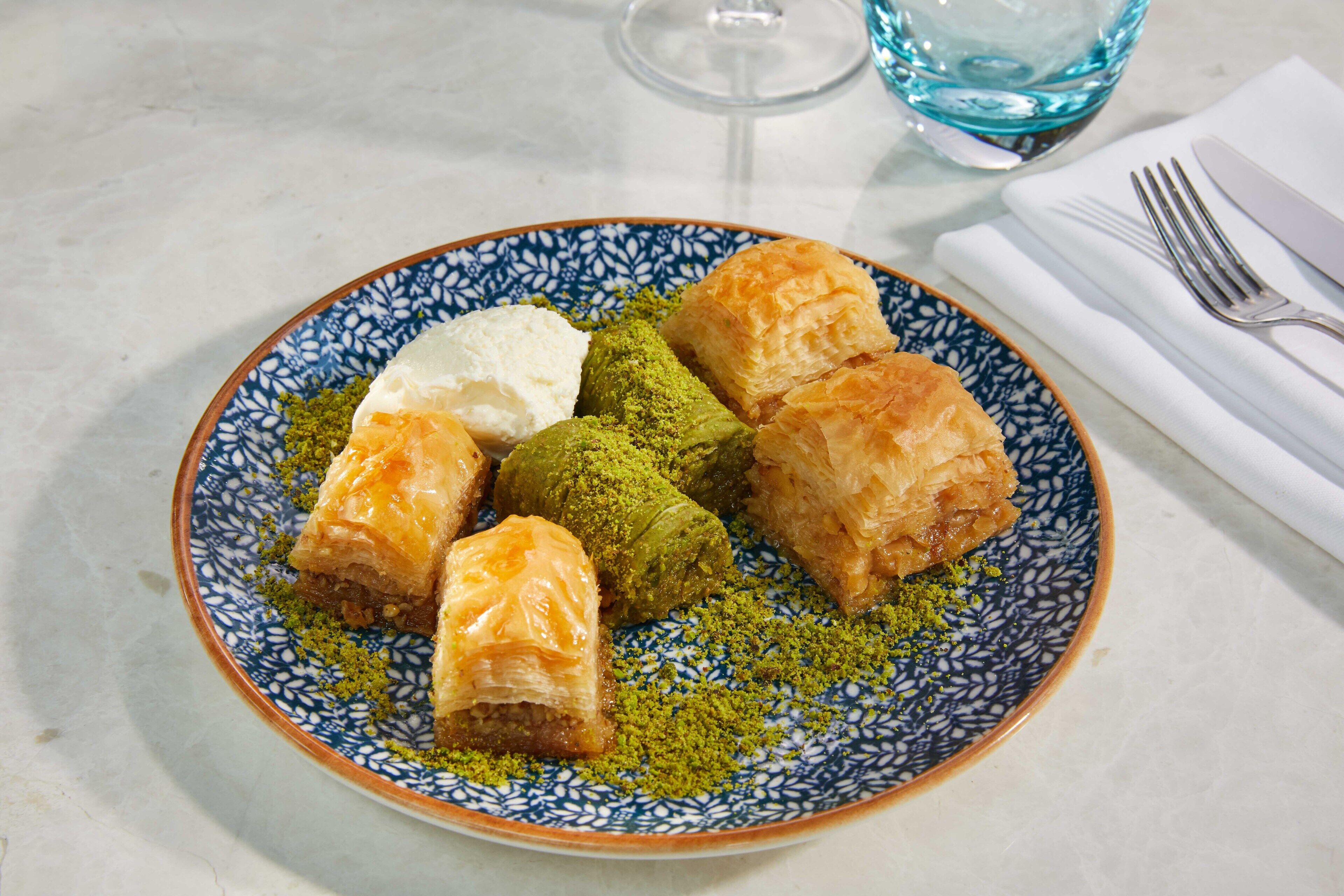 A plate of baklava with pistachios on a blue and white patterned plate.
