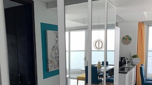 En moderne stue med glasvæg, et spiseområde med blå stole og udsigt til havet.
