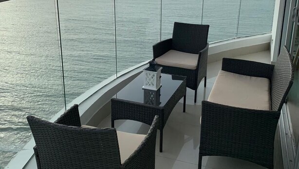 En balkon med fletmøbler og et glasbord, med udsigt over havet.