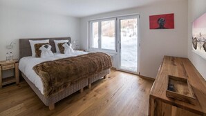 A bedroom with a bed, wooden floor, a bench, a window, and a painting on the wall.