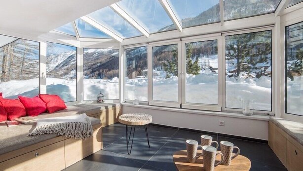 A sunlit room with large windows overlooking a snowy mountain landscape.