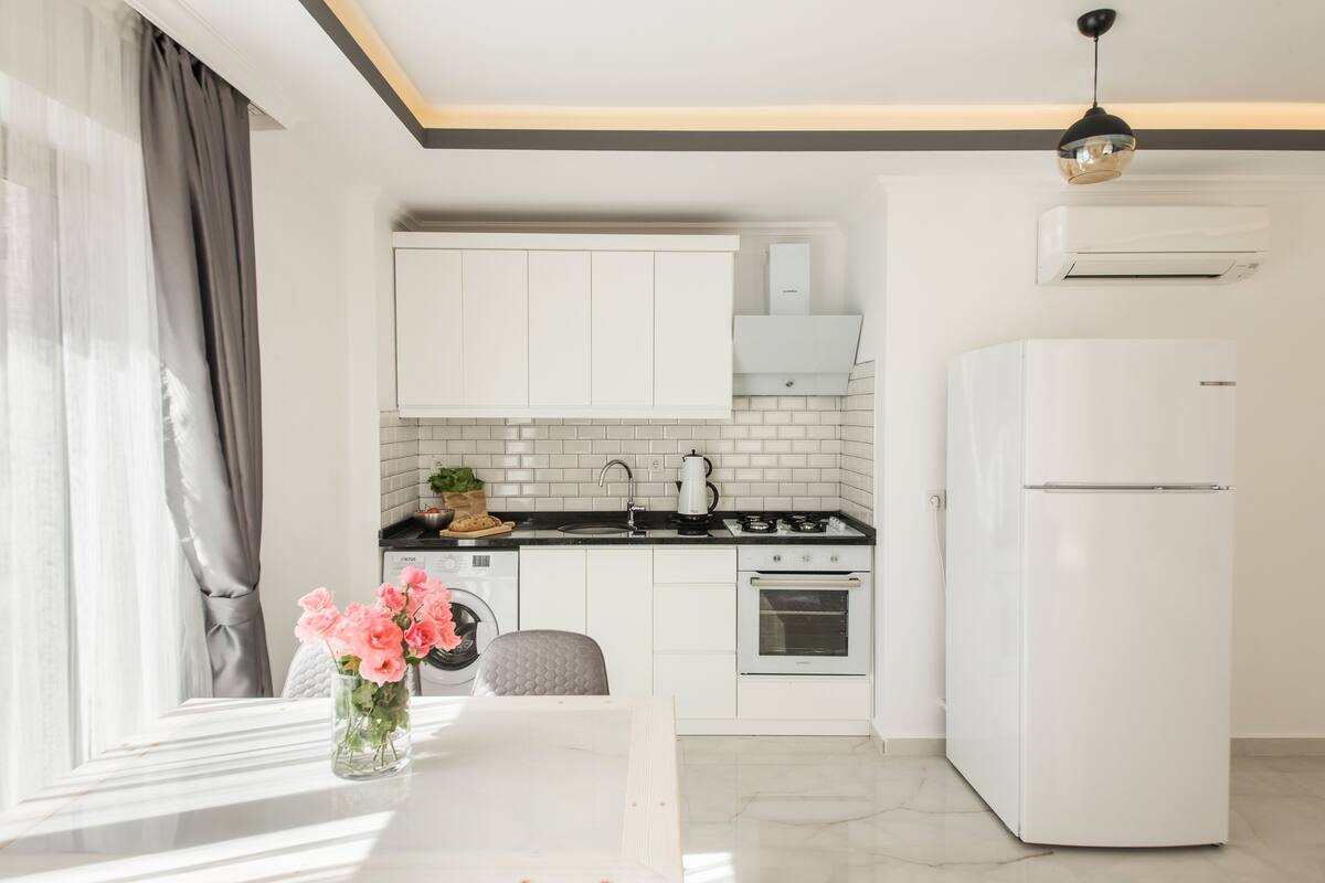 A modern kitchen with white cabinets, a black countertop, and a white refrigerator.