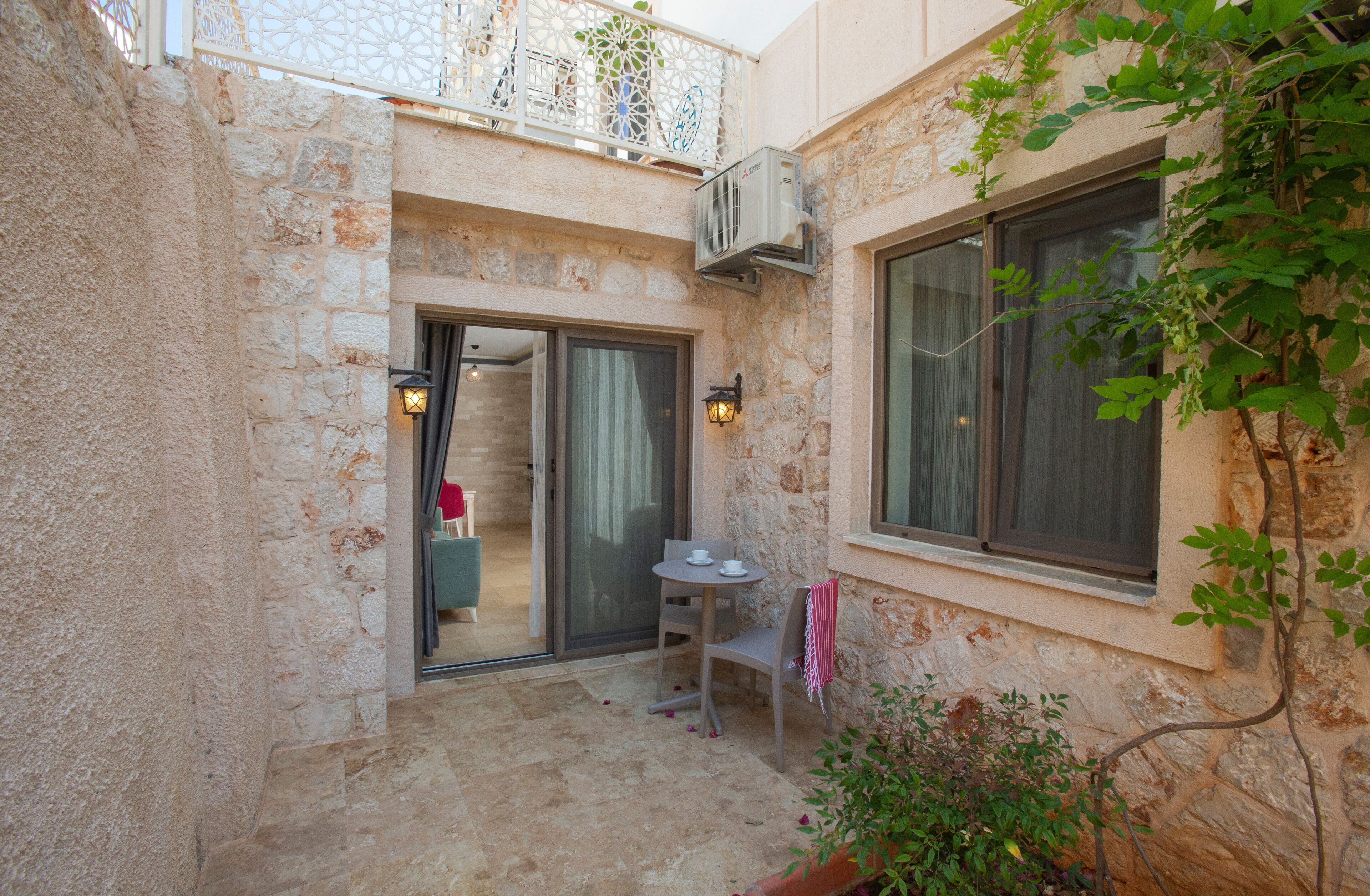 A stone building with a balcony, a small patio with a table and chairs, and a window with a view.