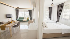 A modern hotel room with a bed, a desk with a chair, a sofa, and a TV. - Cedrus Suites (Kas)