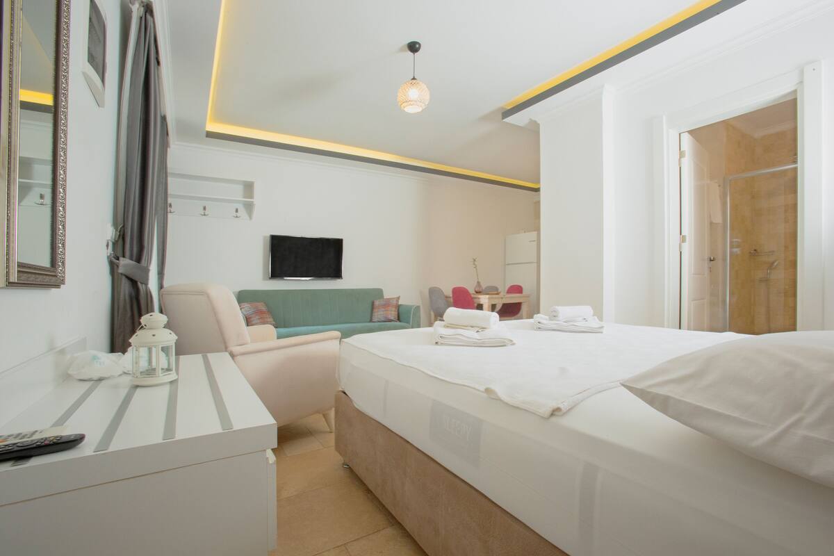 A modern hotel room with a neatly made bed, a desk with a lamp, a chair, and a television on the wall.