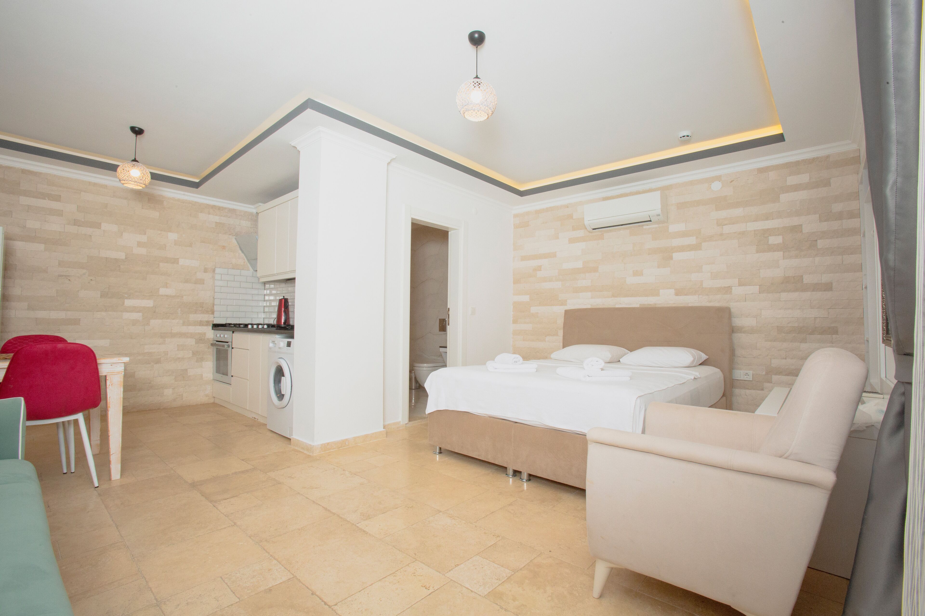 Habitación de hotel pequeña con cama, una silla, una mesita, lavadora y kitchenette.