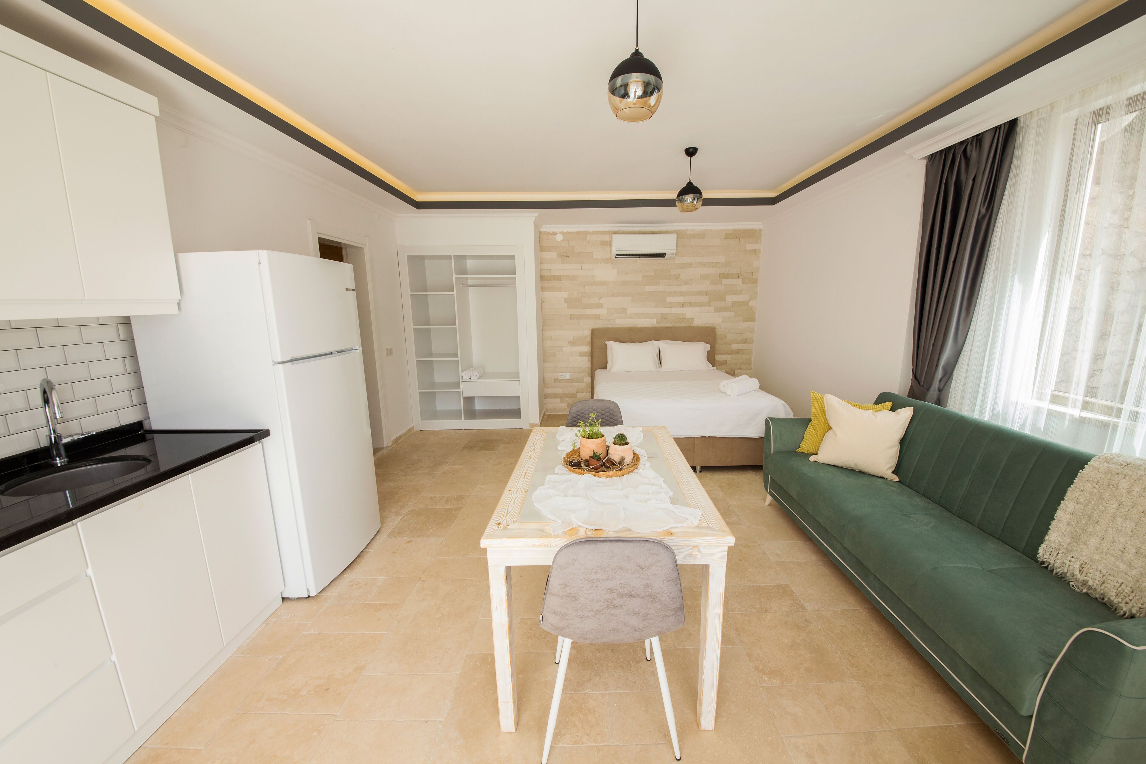 Een ruimtelijk ingerichte leefruimte met kitchenette, een eettafel met stoelen, een groene bank en een bed met hoofdeinde.
