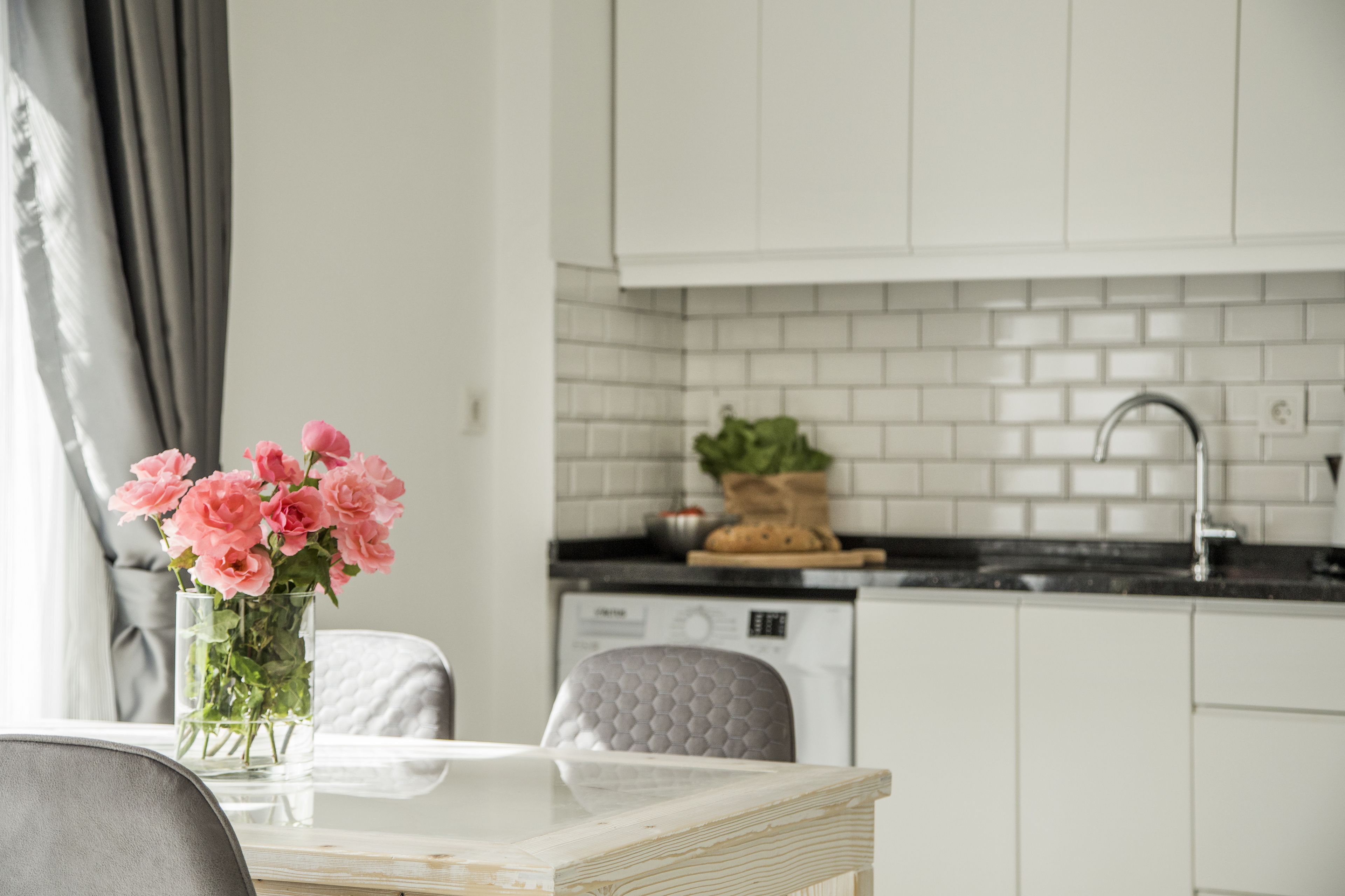A modern kitchen with white cabinets, a black countertop, and a dishwasher. There is a vase with pink flowers on the table.