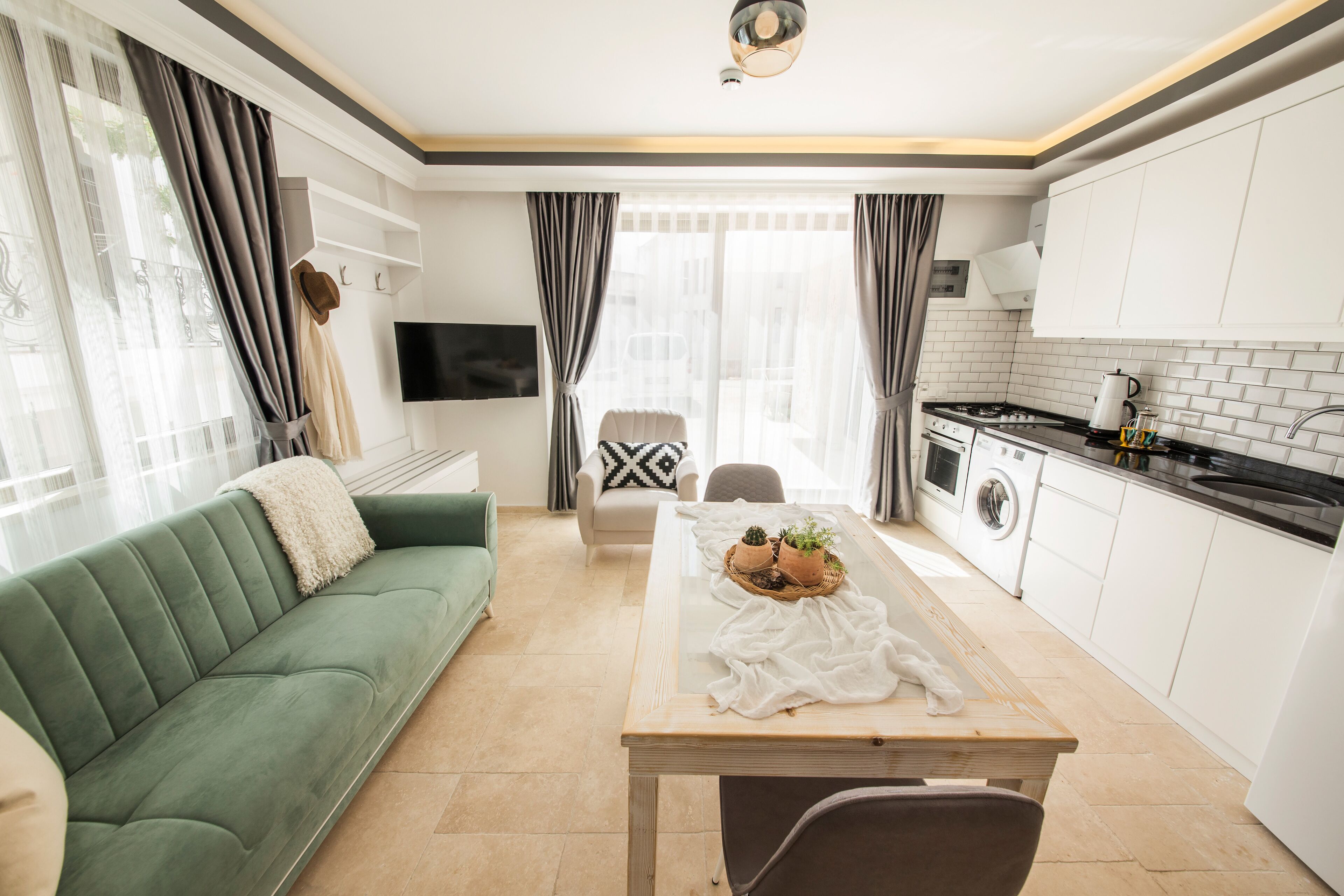 Una sala de estar moderna con un sofá verde, una mesa de comedor con mantel blanco y una cocina con armarios blancos y estufa.