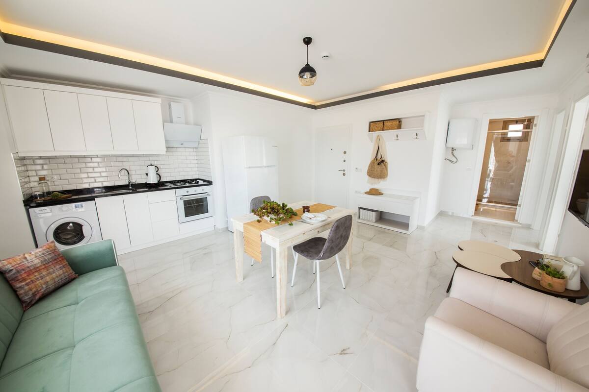 A modern kitchen with white cabinets, a dining area with a table and chairs, and a living area with a sofa and a coffee table.
