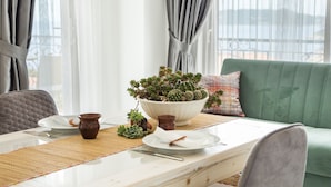 A dining table with a bowl of succulents, a plate, and a cup, set on a balcony with a green couch and curtains. - Cedrus Suites (Kas)