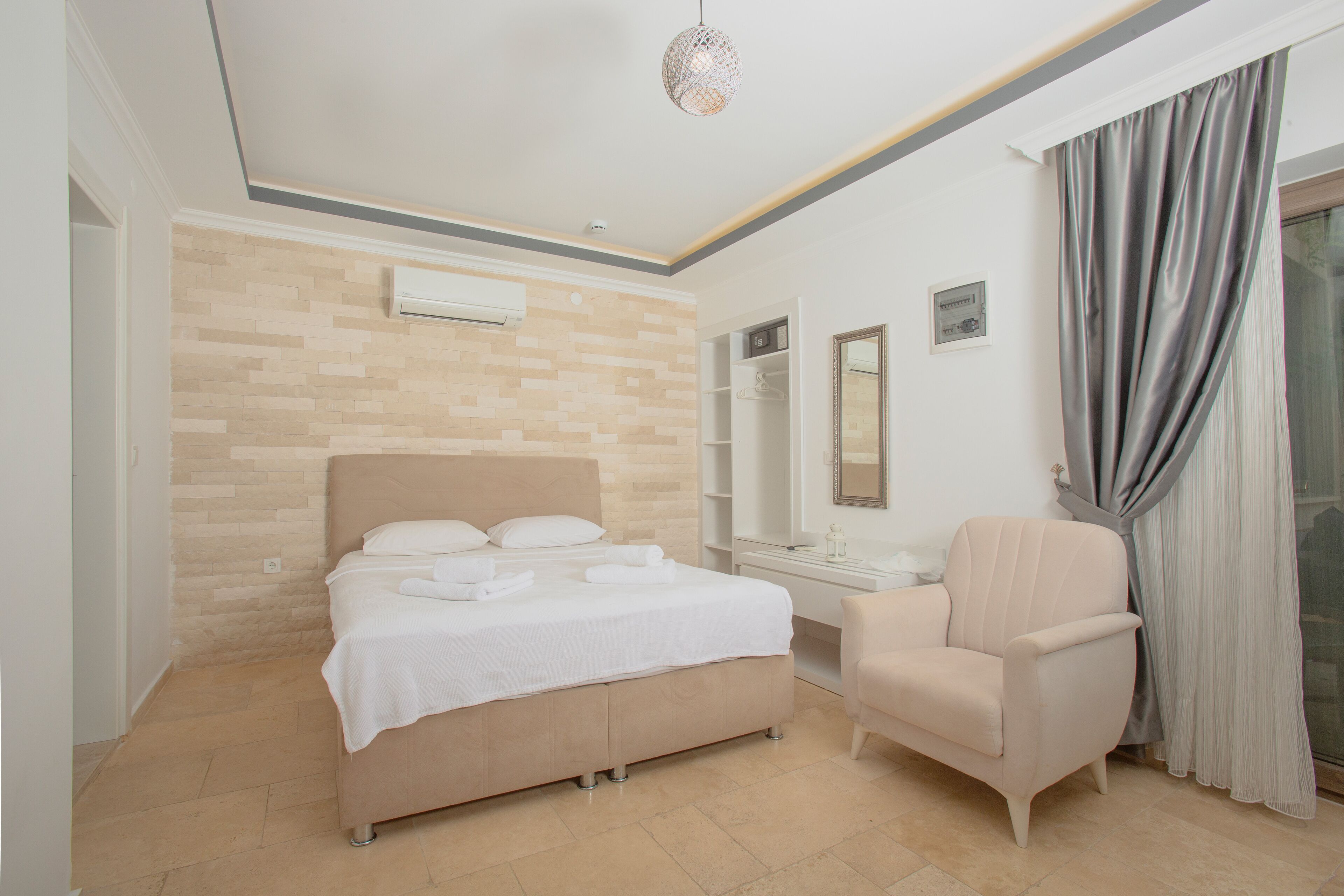 A modern hotel room with a bed, a chair, a vanity with a mirror, and a window with curtains.