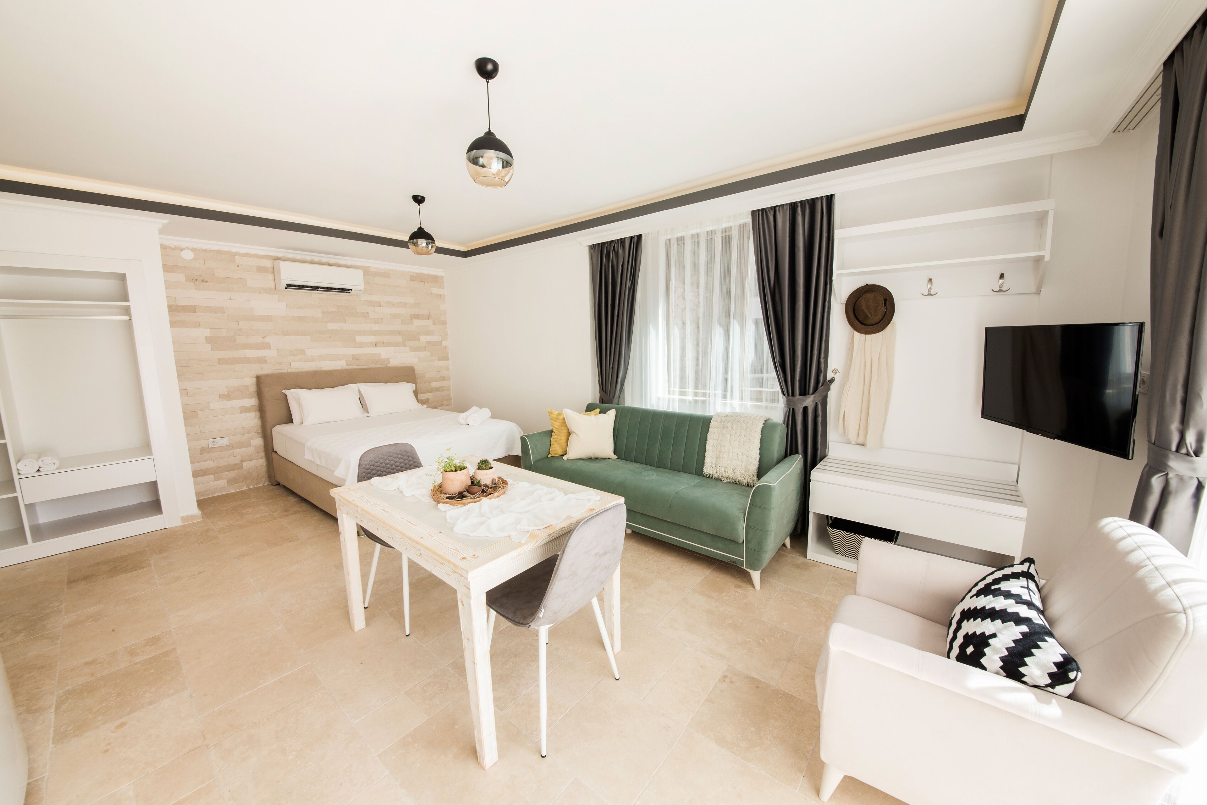 A modern living room with a bed, a green sofa, a white armchair, a dining table, and a TV.