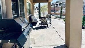 Een overdekt terras met een barbecue, twee stoelen en een kleine tafel.