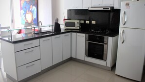 A modern kitchen with white cabinets, a black countertop, a microwave, an oven, and a refrigerator. - Palmetto Eliptic 1002 (Cartagena)