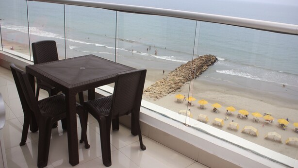 A balcony with a table and chairs overlooking a beach with umbrellas and people. - Palmetto Eliptic 1002 (Cartagena)