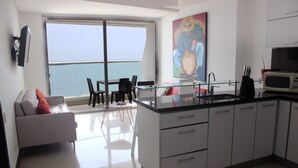 A modern kitchen with a large window, a dining area with a table and chairs, and a living area with a sofa. - Palmetto Eliptic 1002 (Cartagena)
