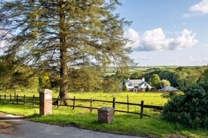 A rural landscape with a large tree, a wooden fence, and a house in the background.