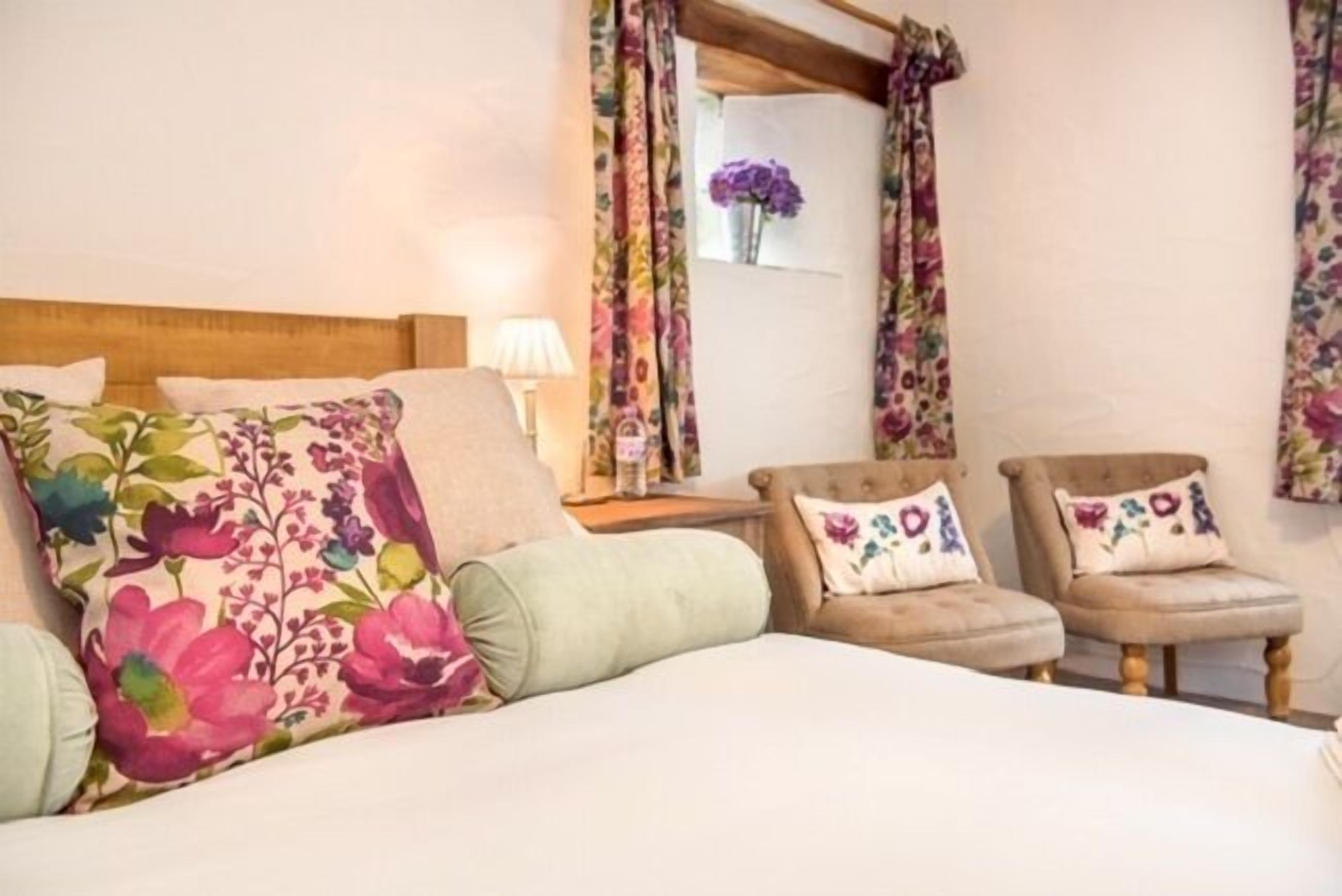 Een hotelkamer met een bed, twee fauteuils, een nachtkastje en bloemenprint gordijnen.