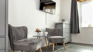 A modern room with two grey upholstered chairs, a small round table with a vase of flowers, a grey dresser, and a large mirror on the wall. - Coombe Farm (Looe)