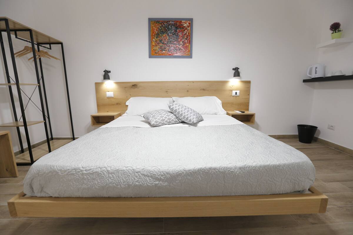 Una cama con estructura de madera, ropa de cama blanca y dos lámparas de noche.