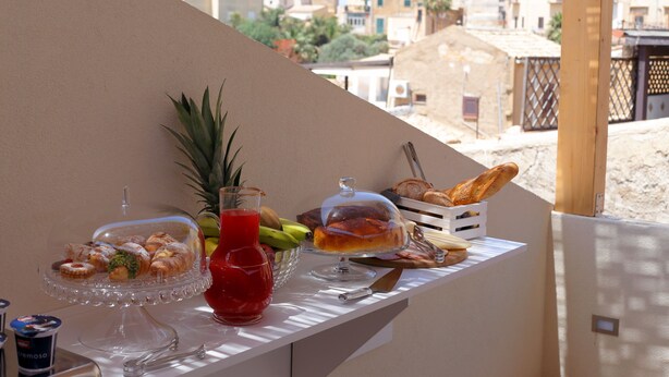 Un bufé de desayuno con pasteles, frutas y una bebida en un balcón con vistas a la ciudad.