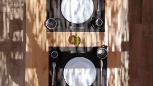 Una mesa de comedor dispuesta con platos, cubiertos y tazas, con un mantel individual y un pequeño adorno en el centro.