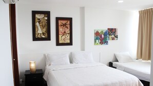 Een hotelkamer met twee bedden, een nachtkastje met een lamp en drie ingelijste kunstwerken aan de muur.